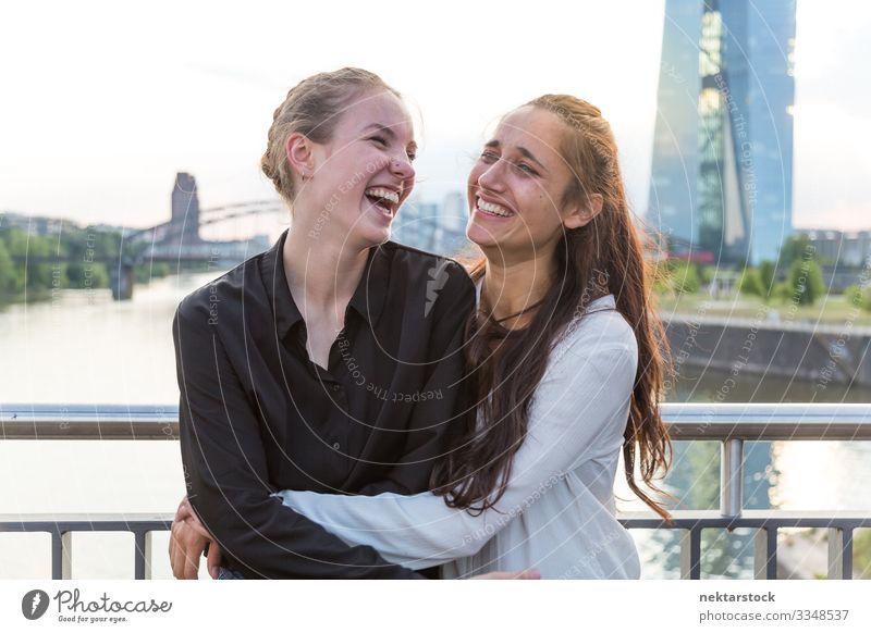 Girlfriends Embracing and Laughing on City Bridge Joy Happy Woman Adults Friendship Youth (Young adults) Youth culture Nature River High-rise Building Laughter
