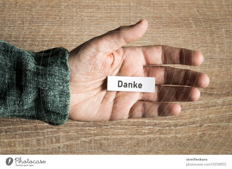 Note with writing "DANKE" lies in the open palm of the hand against a wooden background Success To talk Team Human being Hand Paper Piece of paper Characters