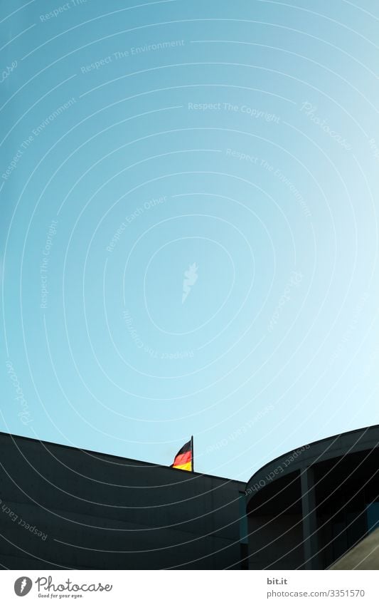 Flag; flag of Germany on a mast, under a blue sky in the government quarter in Berlin, hidden behind a building, in summer during an excursion while on holiday in the capital.