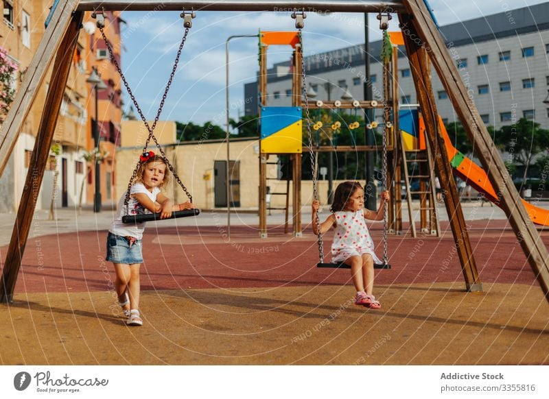 Girls on swing in park girls playground rest summer sit sunny kids weekend children childhood fun little relax lifestyle cute adorable innocence calm tranquil
