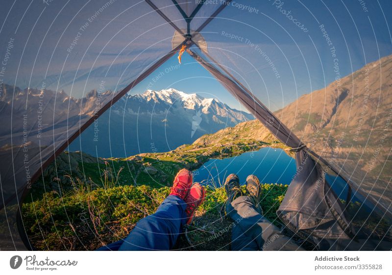 Relaxed tourists lying in tent in snowy mountains in sunlight rock lake reflection crystal clear nature travel relationship tourism camp together friendship