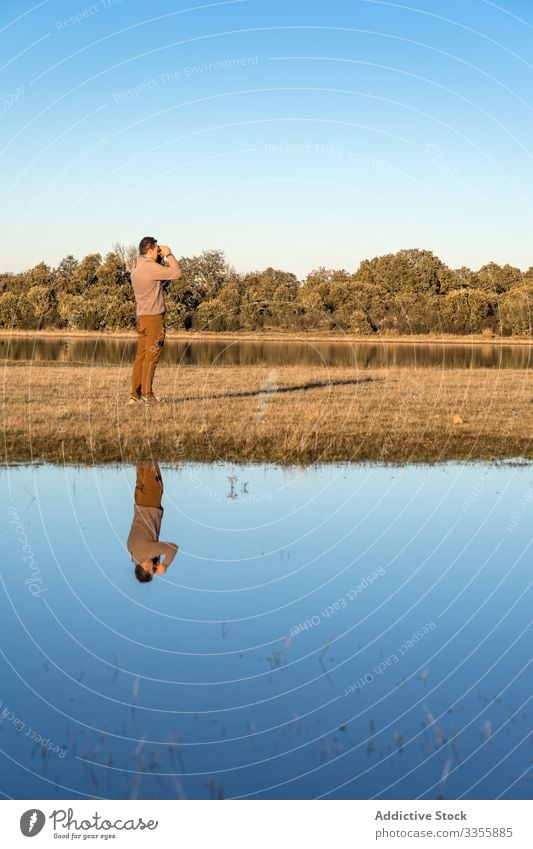 Anonymous man looking on binoculars in a lagoon water landscape forest lake wetland adventure wild fauna blue sky sunny scenic copy space nature natural old