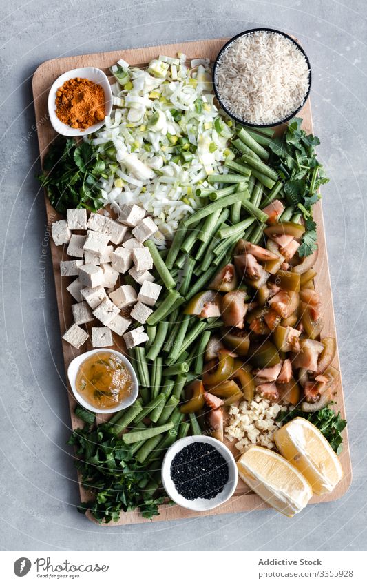 Raw cut meal ingredients on wooden board raw tomato green bean green onion cheese lemon seasoning rice bowl garlic preparation recipe dinner table different
