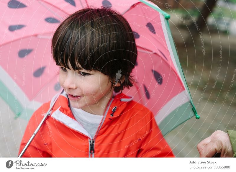 Cute child with colorful umbrella looking at camera in park alley rain season funny water wet dirt childhood mud autumn game active weather rubber boots