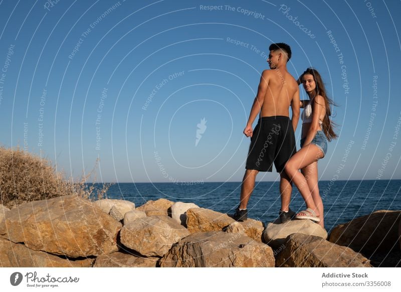 Ethnic male and happy woman standing on stone friend vacation sea beach travel tourist relax ocean together leisure activity smile ethnic adventure destination