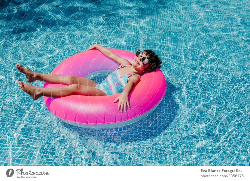 beautiful kid girl floating on pink donuts in a pool. Wearing sunglasses and smiling. Fun and summer lifestyle Action Swimming pool Beauty Photography