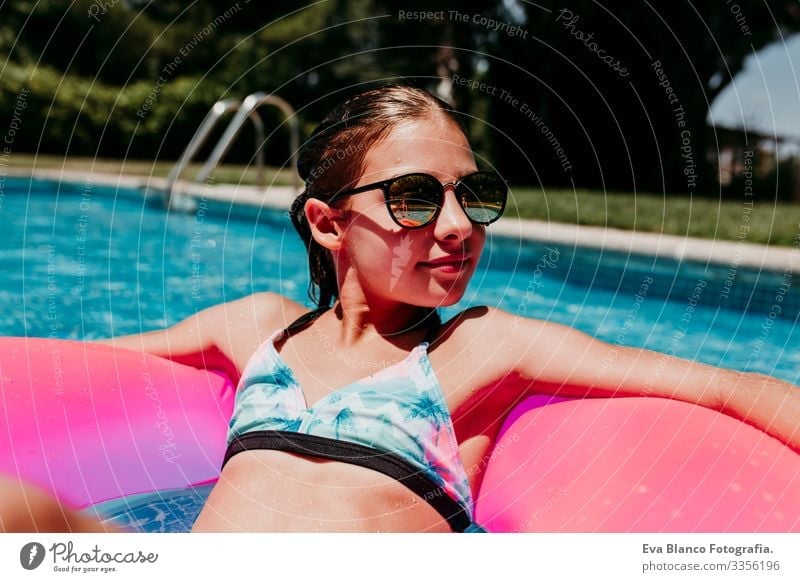 beautiful teenager girl floating on pink donuts in a pool. Wearing sunglasses and smiling. Fun and summer lifestyle Action Swimming pool Beauty Photography