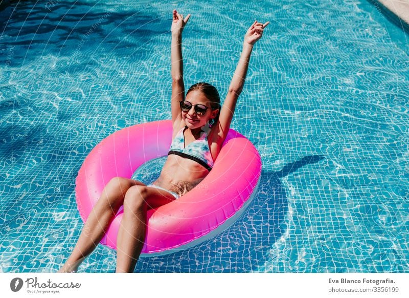beautiful teenager girl floating on pink donuts in a pool. Wearing sunglasses and smiling. Fun and summer lifestyle Action Swimming pool Beauty Photography