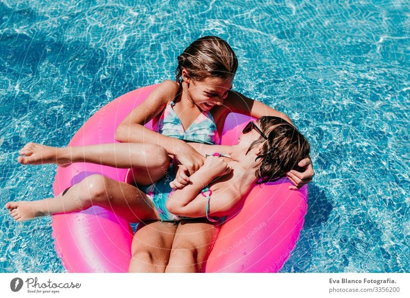 two beautiful sisters floating on pink donuts in a pool. Playing tickles and smiling. Fun and summer lifestyle Action Swimming pool Exterior shot