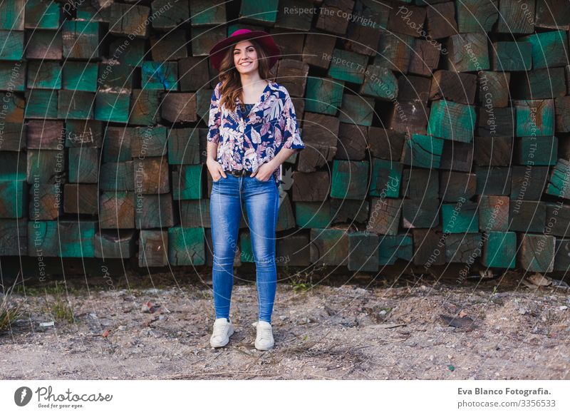 portrait of a young beautiful woman wearing casual clothes and a modern hat, standing over green wood blocks background and smiling. Outdoors lifestyle.