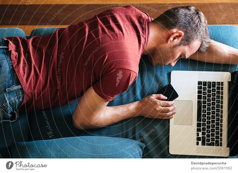 Tired guy sleeping on sofa with devices at home man asleep couch tired freelance living room overworked smartphone mobile laptop exhausted nap modern young male