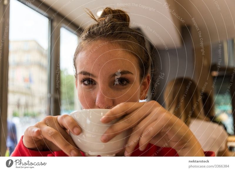 Young Woman Drinking from Coffee Mug and Looking at the Camera female girl coffee cup woman young adult face day female beauty beautiful woman natural beauty