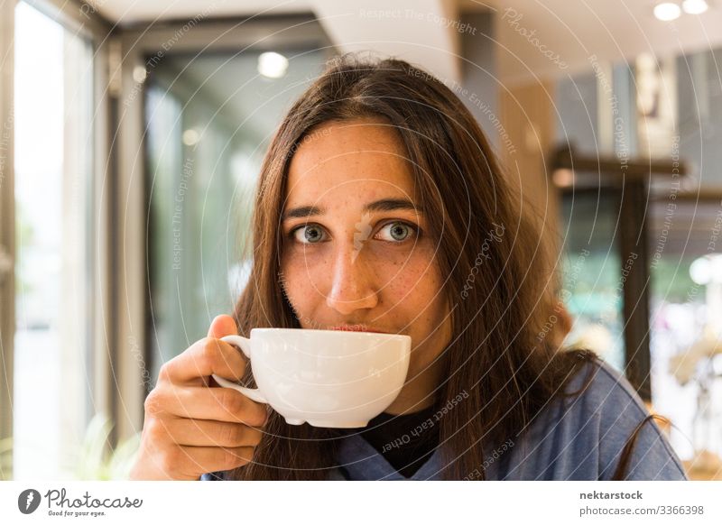 Young Woman with Coffee Mug on Lips Looking at Camera Portrait female tanned skin light colored eyes coffee cup mug drinking beverage porcelain
