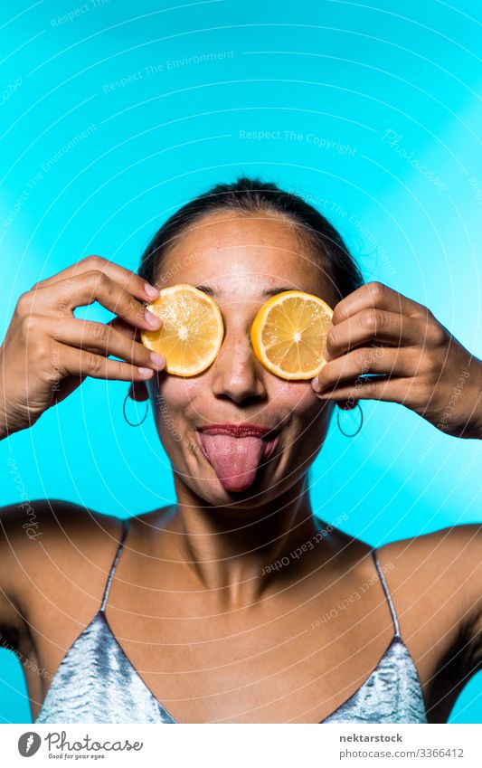 Young Woman Covering Eyes with Lemon Slices and Sticking Out Tongue lemon slice female tongue out girl eyes holding up concept sticking out tongue minimalism