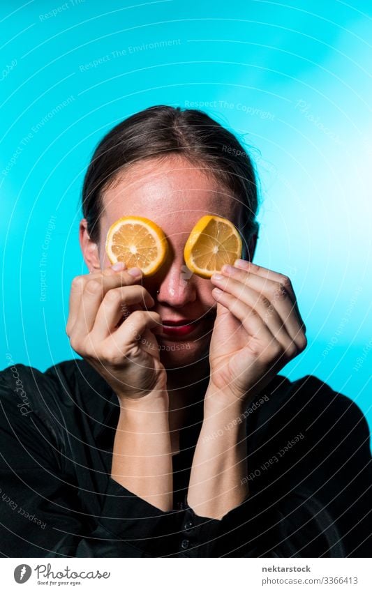 Young Woman with Lemon Slices Over Eyes on Blue Background lemon slice covering female girl eyes holding up concept minimalism citrus fruit fresh freshness