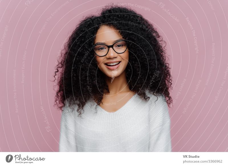 Portrait of beautiful Afro American woman with crisp hair, dressed in  elegant black jacket, transparent glasses, looks directly at camera with  gentle smile wears optical glasses isolated on brown wall - a