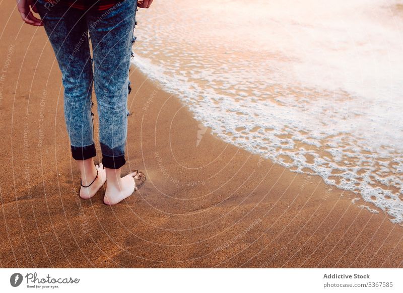 Woman dressed in jeans standing on beach woman barefoot barefooted hipster sea sand stormy wear female style personality ocean water nature travel coast seaside