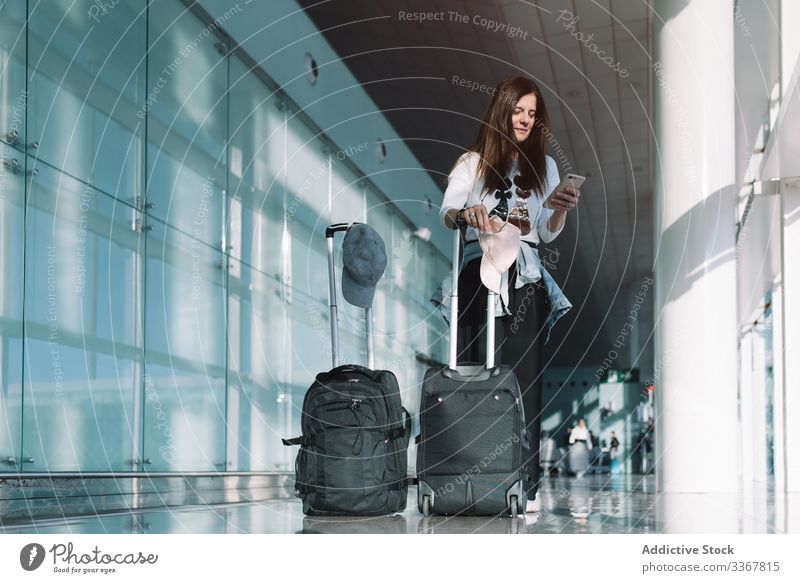 Calm woman using phone in airport surfing baggage vacation departure arrival adventure female wait smartphone delay public destination browsing explore holiday