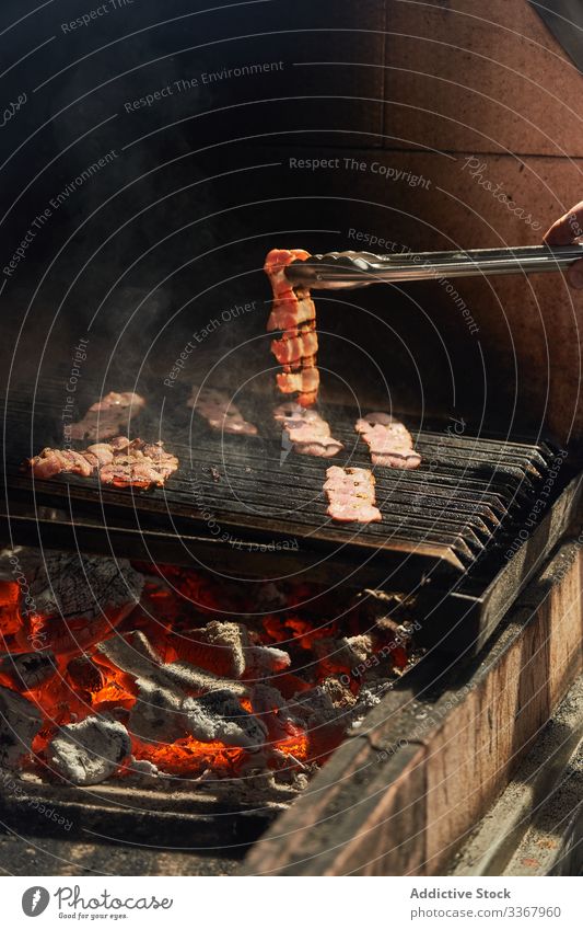Faceless man turning slices of bacon on grill rack chef barbecue flip tongs cook garden fried meat food preparation meal dish heat cookery lunch cuisine fresh