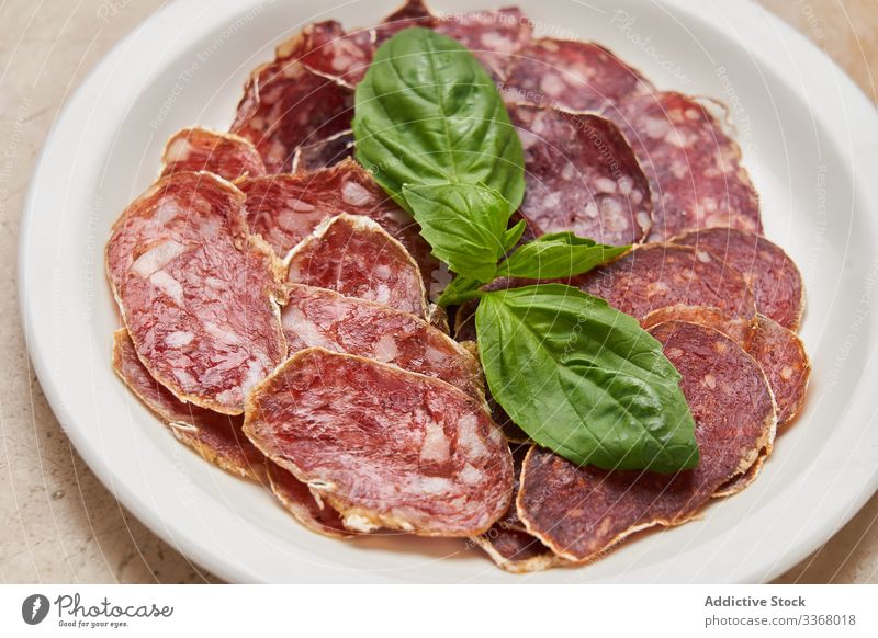 Pieces of dried meat with basil sausage slice snack smoked green leaves service decoration plate dish simple restaurant herb stylish elegant luxury salami