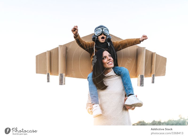 Cheerful mom and son playing together in field woman aviator dream game fly boy wear goggles wing mother imitate meadow cardboard on shoulders child parent kid