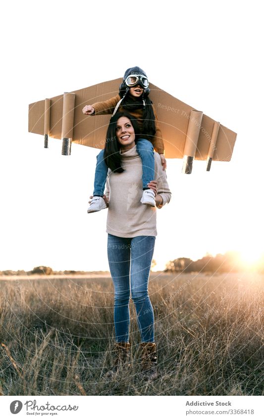 Cheerful mom and son playing together in field woman aviator dream game fly boy wear goggles wing mother imitate meadow cardboard on shoulders child parent kid