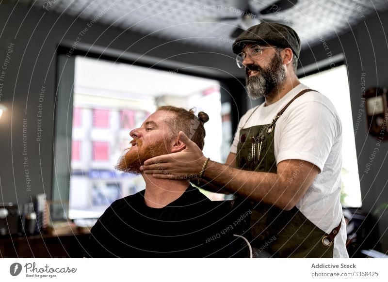 Barber doing face massage to man client trendy hairdresser barbershop beard masculinity young care salon hairstylist handsome stylish relaxing stress relief