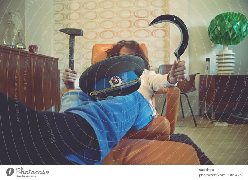 man lying on an armchair with russian cap on his knees and holding sickle and hammer in his hands . Man Living room couch Armchair Retro sedentary reclining