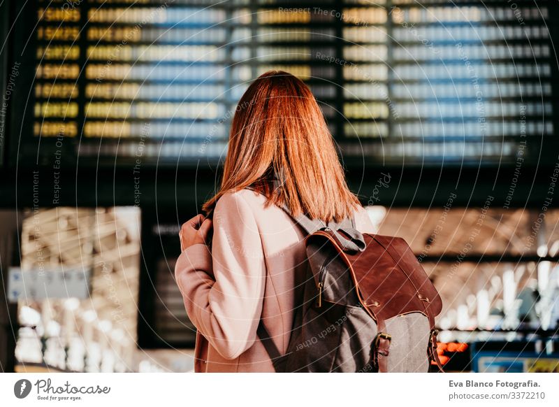 young woman at train station looking at destination board. Travel and public transport concept screen travel backpack back view caucasian europe railway waiting