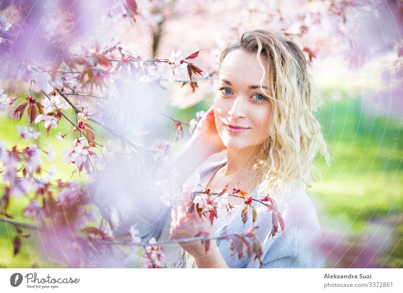 Young woman enjoying the nature in spring. Breathing fresh air and flowers aroma in beautiful park with cherry trees in bloom. Happiness concept Beautiful