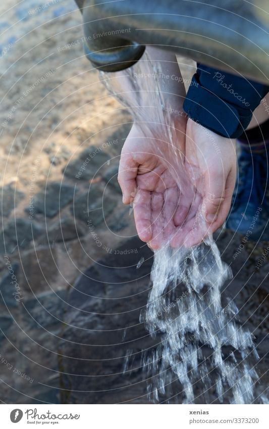 Hands in the jet of the water pump with a view of blurred cobblestones Drinking water by hand 1 Human being Water Water pump Jet of water Fresh Wet Gray