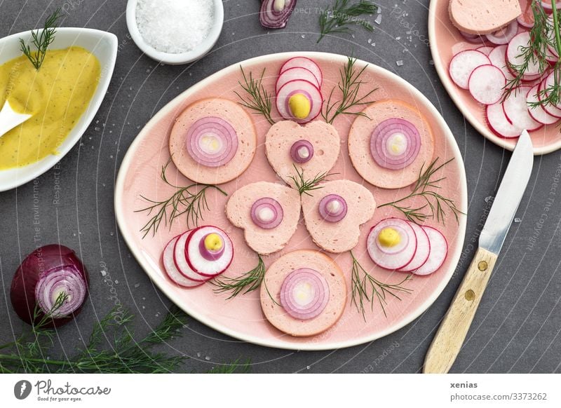 Sausage salad with radish, dill, onion and mustard sauce arranged on pink plates, served with coarse salt and knife with wooden handle sausage Lettuce Meat