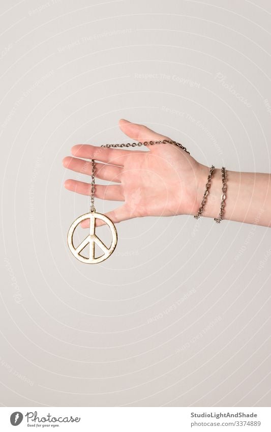 Female hand holding peace sign pacific arm fingers female girl woman young hippie youth gold golden gray grey pink white chain bracelet jewelry metal metallic