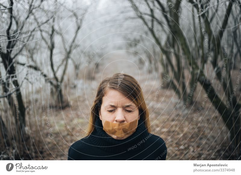 Woman with tape on her mouth in cold winter forest adult anxiety behavior blond caucasian censorship civil concepts depression despair distraught emotional