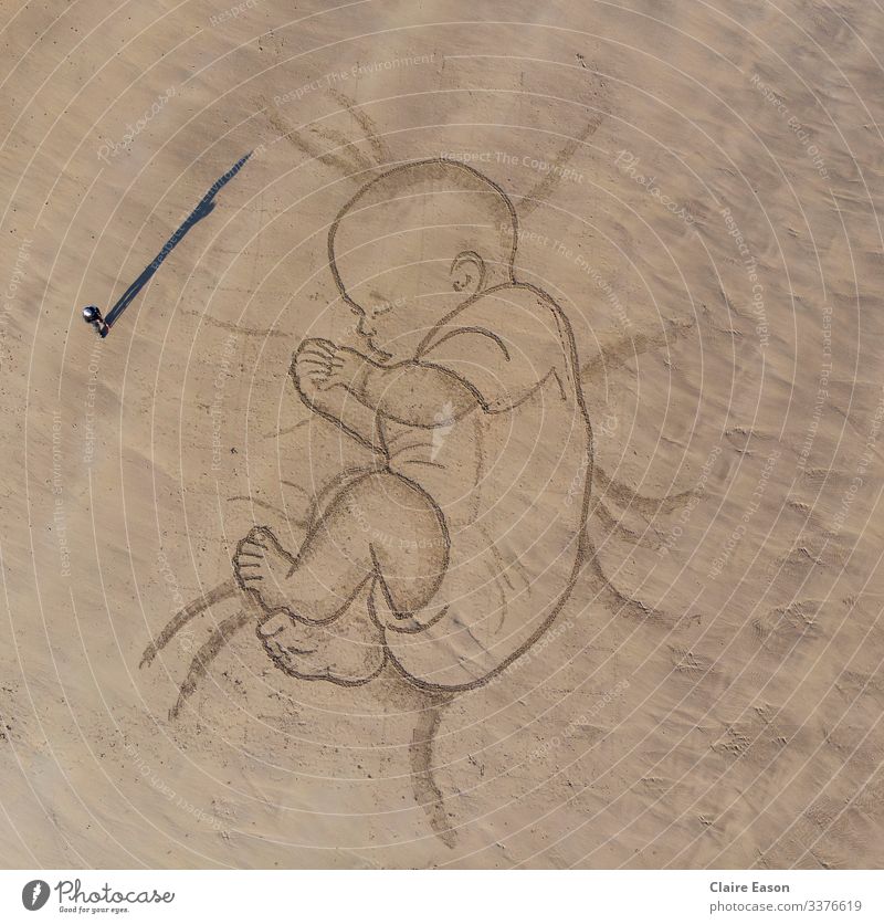 Giant sand art drawing of a sleeping baby with person for scale peaceful parenthood family beach coast environment sustainability Ecotourism