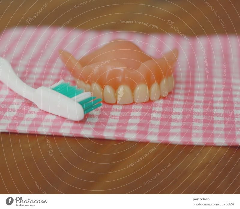 Tooth prosthesis and toothbrush rest on chequered fabric on wooden table Teeth Retro Clean Checkered Napkin Pink Replication Toothbrush Study Practice Cavities