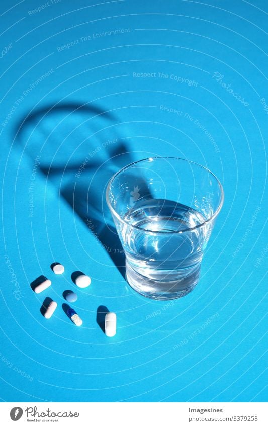 Glass of water and vitamins, pills and tablets on blue background with text Free space Water Text Free Space antibiotic aspirin Capsule Close-up concept