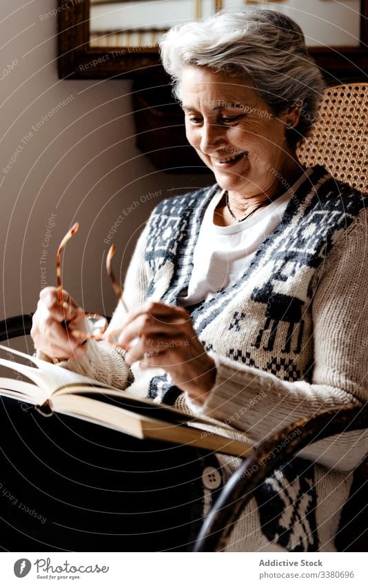 Elderly woman smiling with glasses and open book on knees in armchair smile elderly literature concentrate information intelligent smart creative relax peaceful