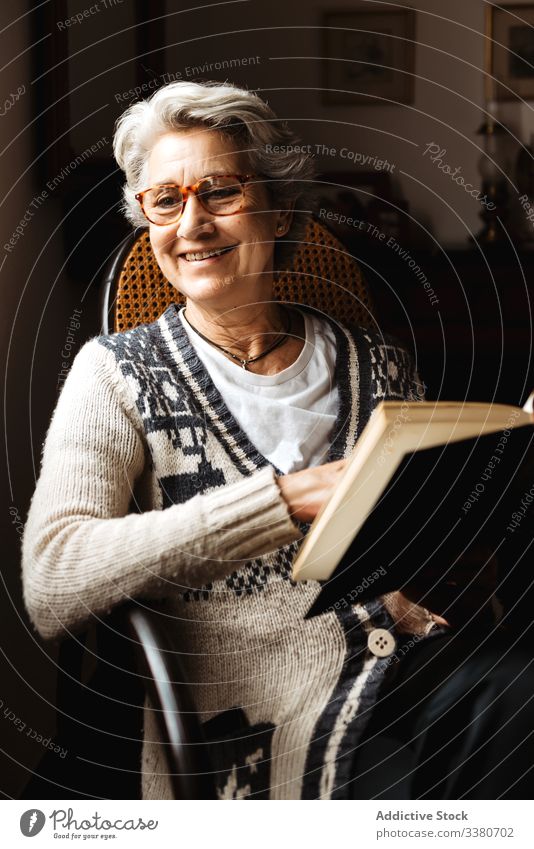 Elderly woman reading by window with enthusiasm book elderly knowledge literature concentrate information intelligent smart creative glasses relax hobby