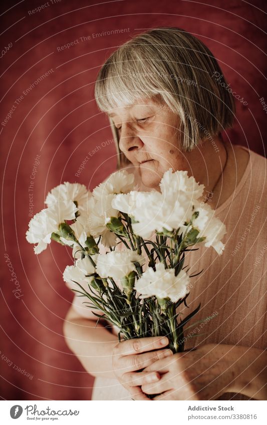 Pensive elderly woman with flowers at home old carnation bouquet floral natural gift fresh female spring celebrate fragrant event holiday festive peaceful