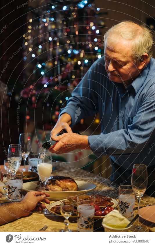 Old man pouring champagne in glasses during Christmas dinner at home christmas celebrate bottle aged senior casual drink beverage male alcohol lifestyle