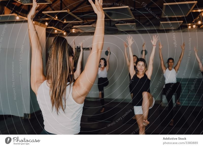 Group of calm focused women and men practicing yoga with trainer standing in balance pose and stretching body in studio instructor practice class fitness