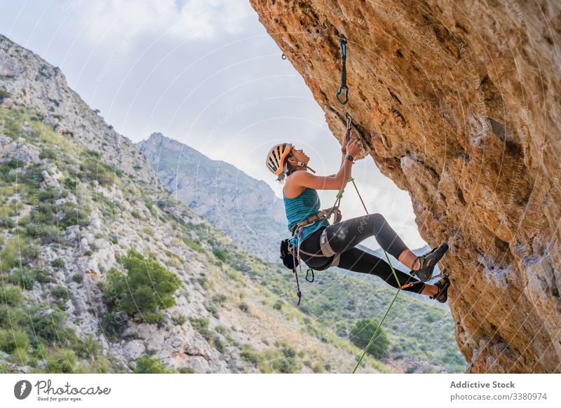 Concentrated young female climber ascending on cliff in summer woman alpinist mountain practice climbing active mountaineering risk travel brave adventure