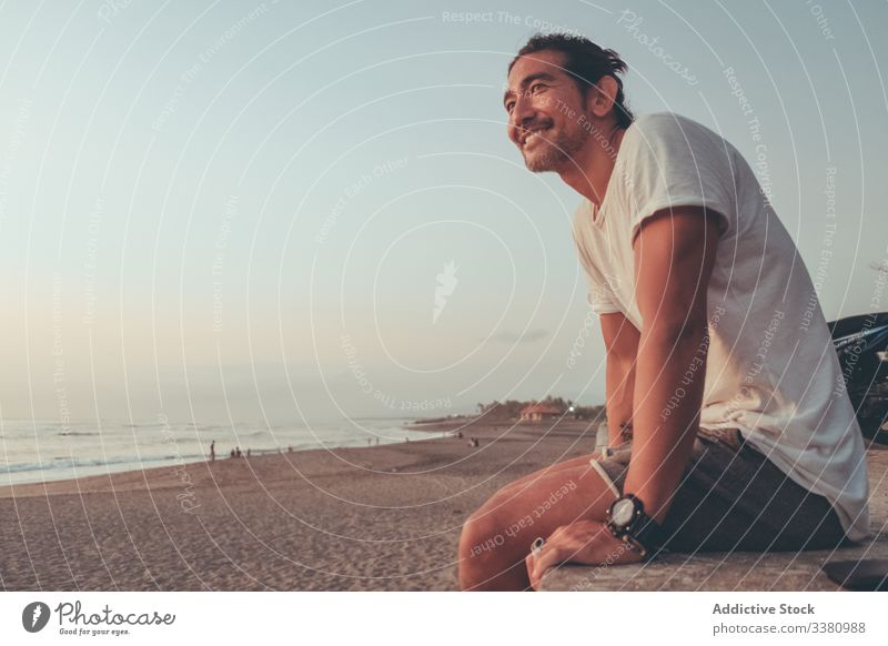 Happy man with motorbike enjoying sunset on beach happy relax sea ocean sit male cheerful positive casual rest lifestyle sand shore coast nature sky dusk