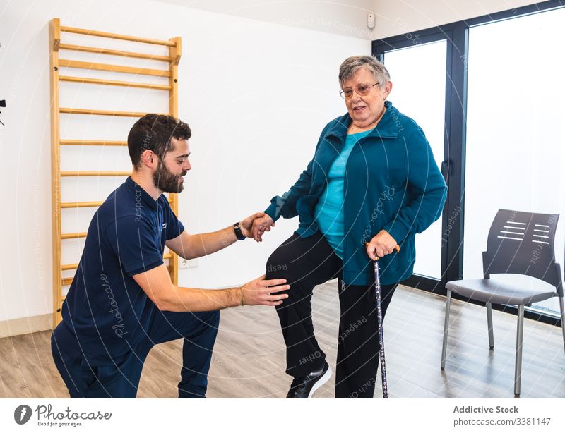 Male instructor supporting old woman using train in gym trainer physiotherapy senior recovery exercise personal male female aged elderly help knee cane fitness