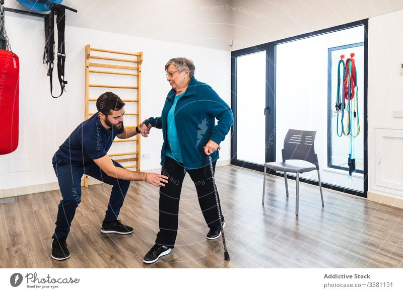 Male instructor supporting old woman using train in gym trainer physiotherapy senior recovery exercise personal male female aged elderly help knee cane fitness