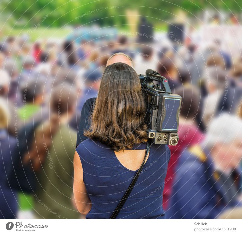 Reporter with camera films man with light hair in front of a crowd of people Rear view rear view from behind Filming Woman Halfway around Long-haired black hair
