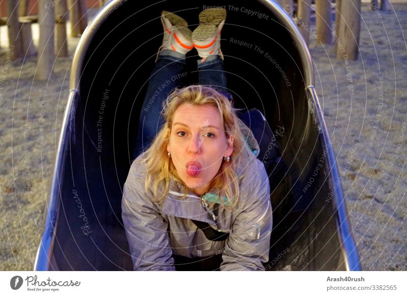 young naughty woman on the slide sticking out tongue Young woman Woman impertinent look Tongue Face eyes Nose Mouth face reclining Slide Playground Game option