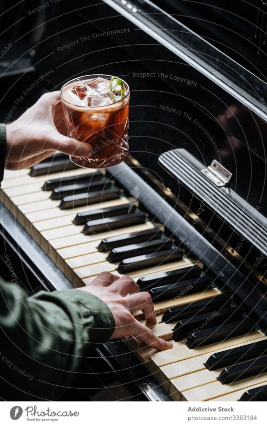Unrecognizable man practicing piano with glass of cold beverage in hand play drink cocktail pub restaurant bar ice mint foam professional fresh classic relax