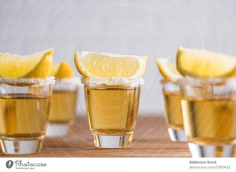 Shots of alcohol with slices of lemon on top shot tequila piece booze row glass table wooden wall drink beverage refreshment tasty cold orange citrus bar juice